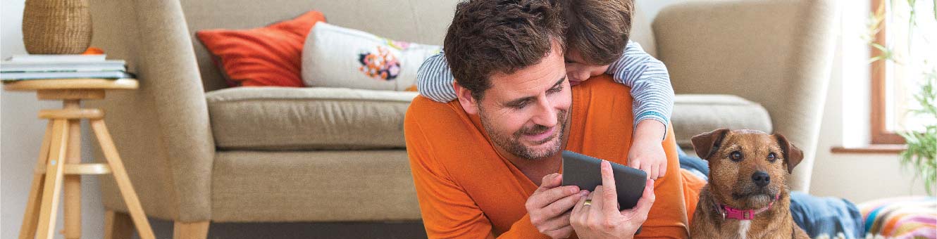 Father and son lying in the floor playing with a mobile phone.