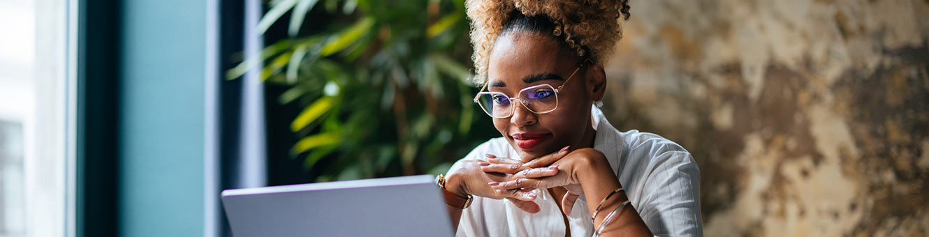 Woman looking at laptop in well lit room with plants.