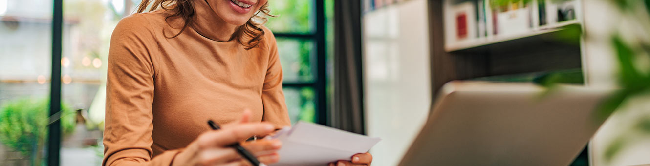 Woman with envelopes and paper at desk in front of laptop.